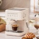 White and beige popcorn maker with glass bowl on top, sitting on a wooden surface with scattered popcorn and a small bowl of