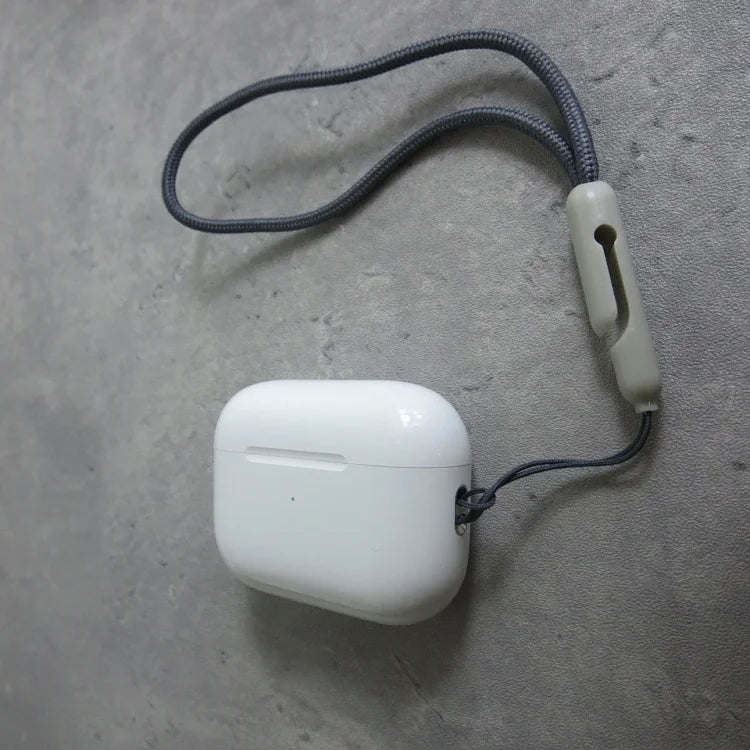 White AirPods Pro case with gray braided cord attached to beige silicone loop, displayed on gray textured surface.