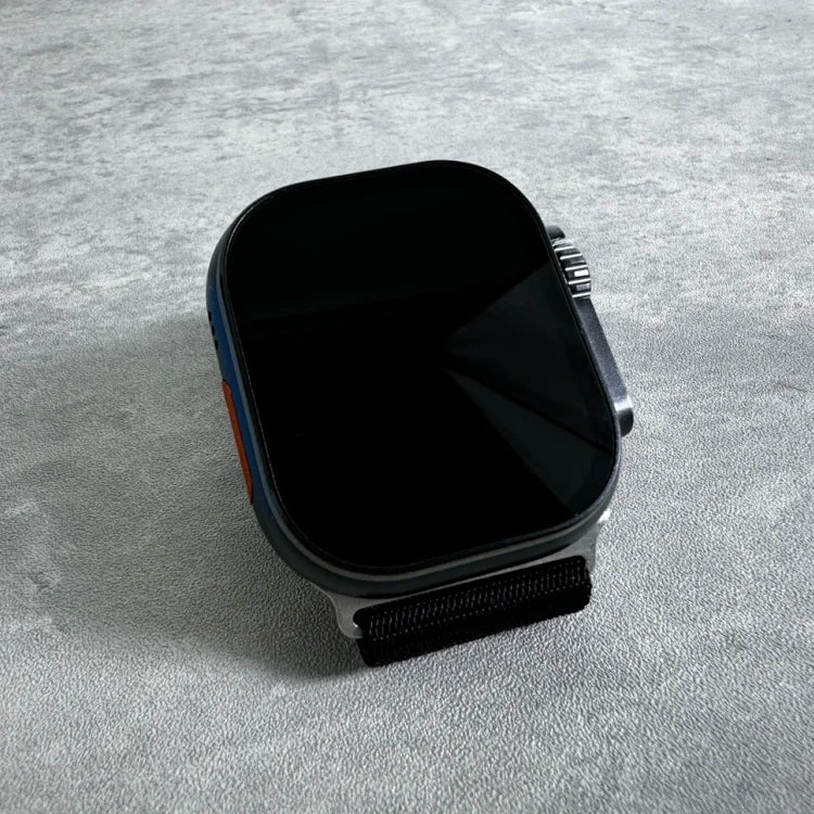 Smartwatch with black square face and dark band displayed at an angle on gray textured surface, showing powered-off dark