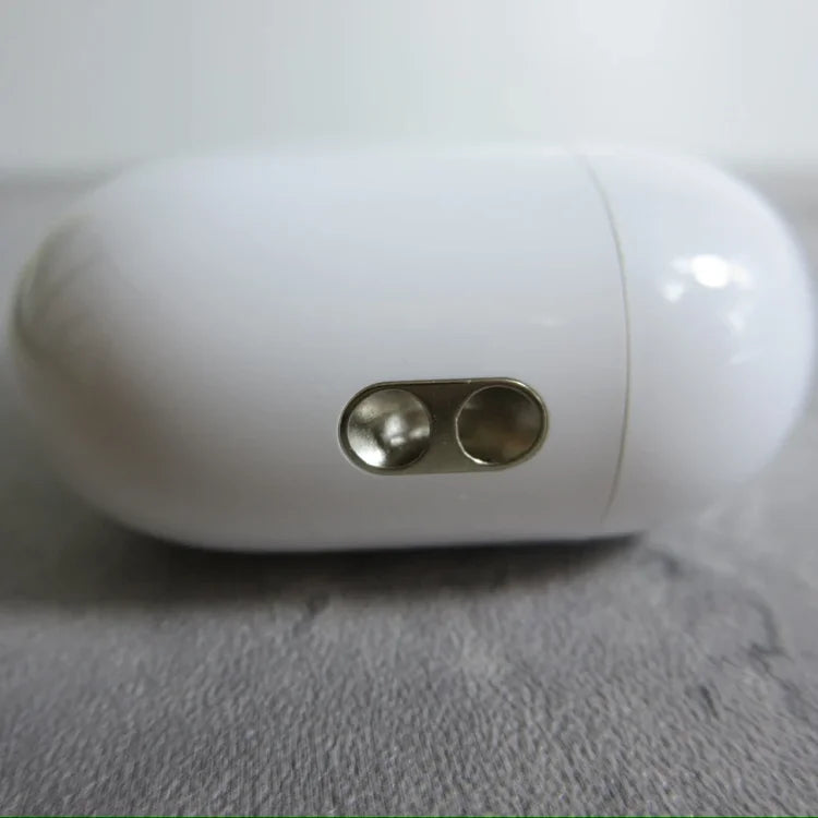 White cylindrical wireless earbud case with two metallic button controls on front, placed on gray fabric surface.