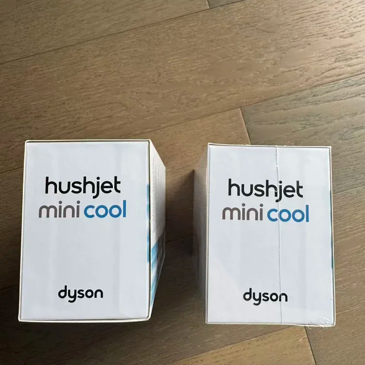 Two white cardboard boxes labeled "hushjet mini cool" by Dyson sitting side by side on a light wood floor.