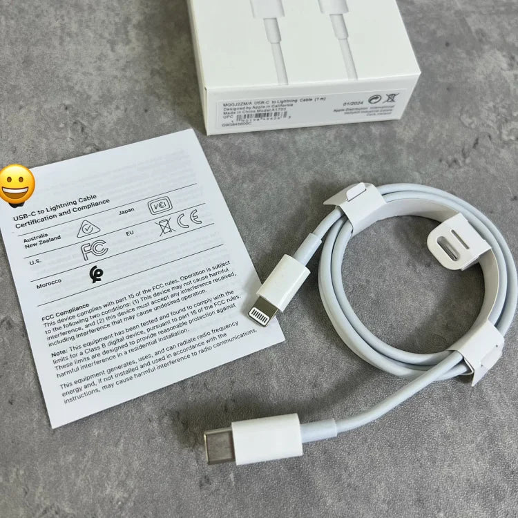 White USB-C to Lightning charging cable coiled on gray surface with instruction manual and retail box visible above.