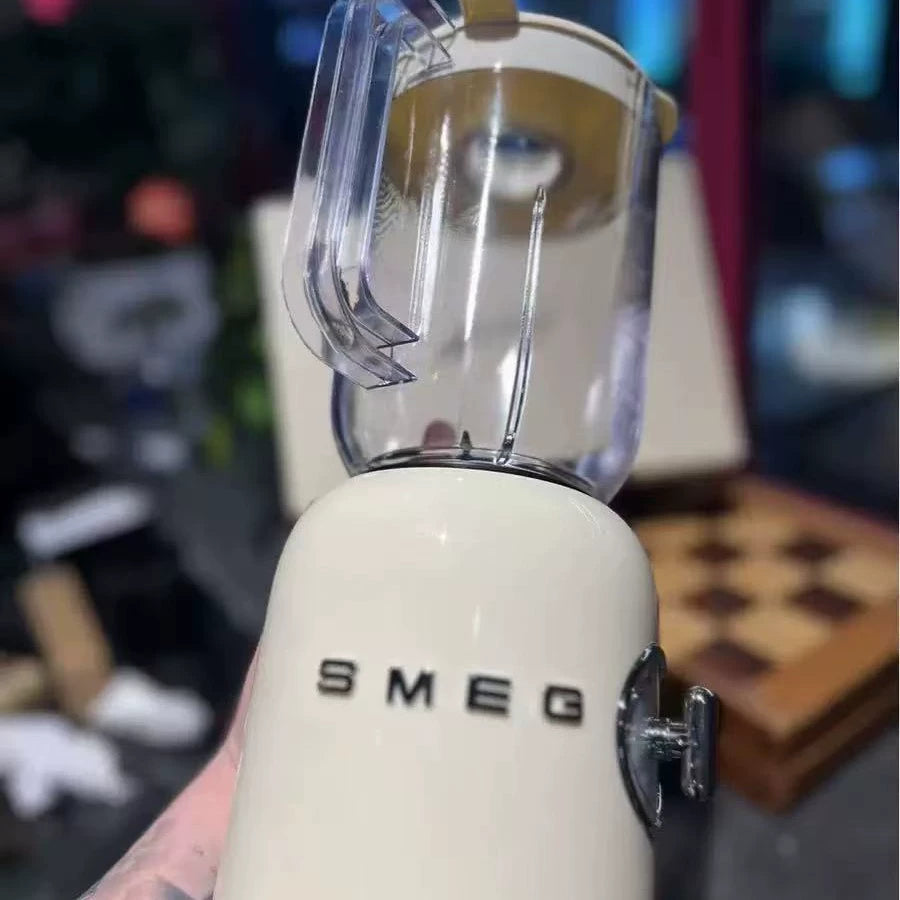 White SMEG brand blender with clear glass pitcher containing pale liquid, shown in close-up with blurred kitchen background