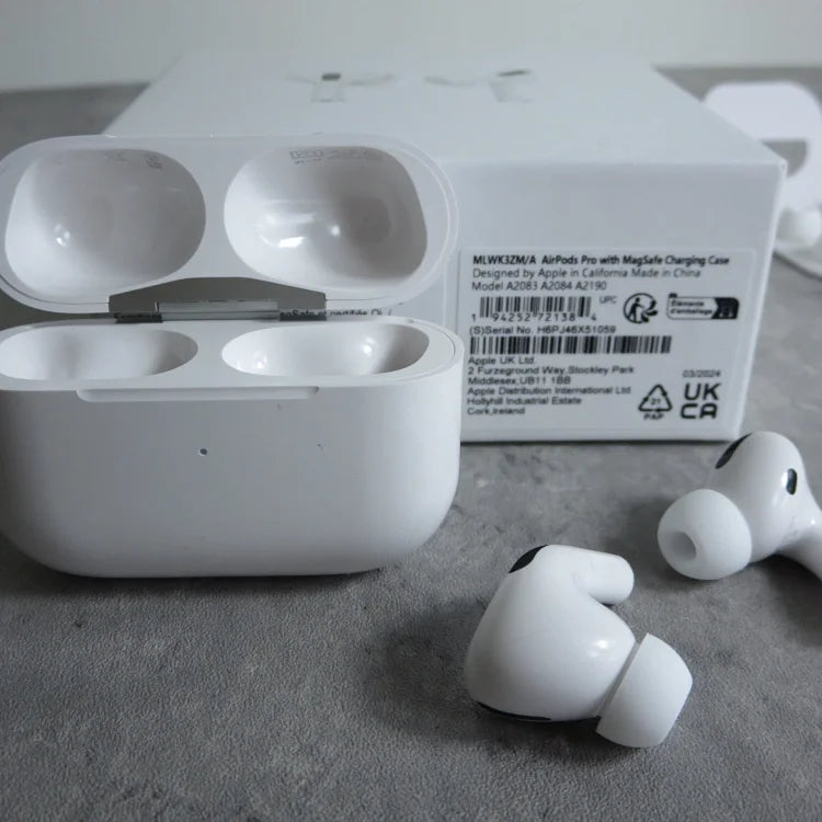 White Apple AirPods Pro with MagSafe charging case, two individual earbuds, and product label visible on gray surface.