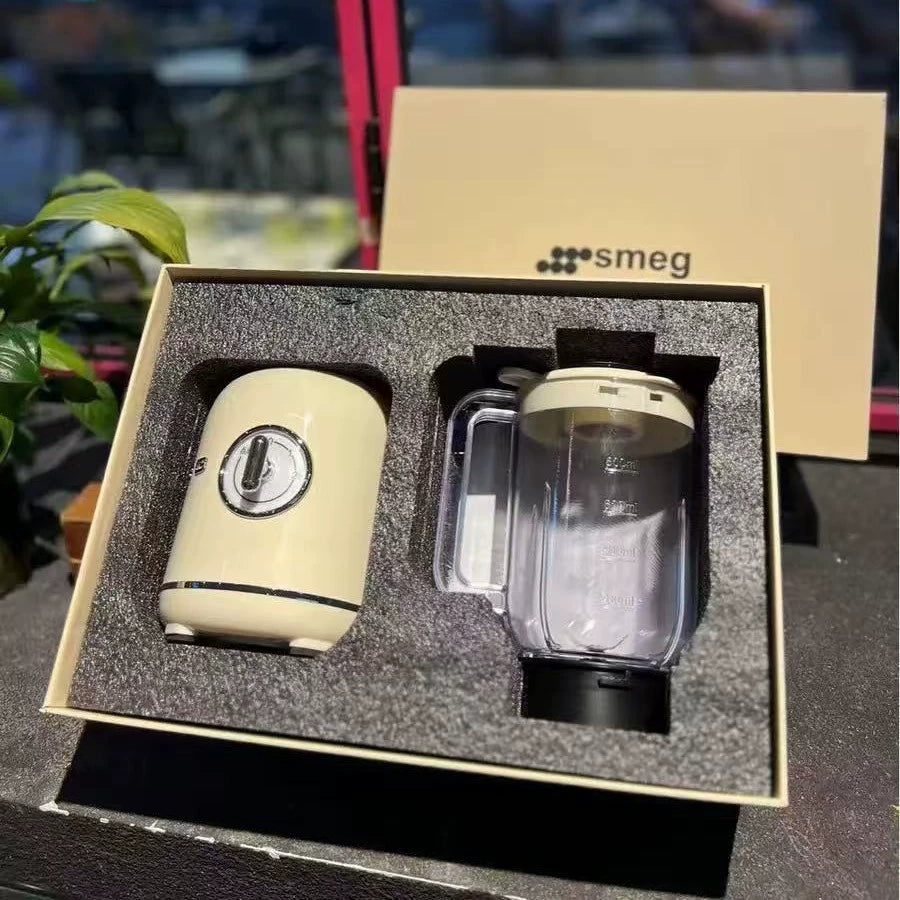 Cream-colored electric milk frother with control dial next to a clear glass blending pitcher, displayed in a beige box with