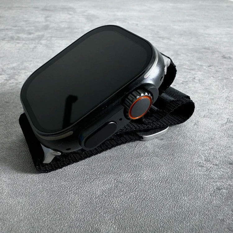 Black smartwatch with rectangular OLED display and orange accent button, mounted on black fabric wrist strap, photographed