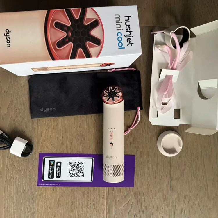 White cylindrical Dyson device with pink rose-gold fan head, displayed with black pouch, charging cables, instruction