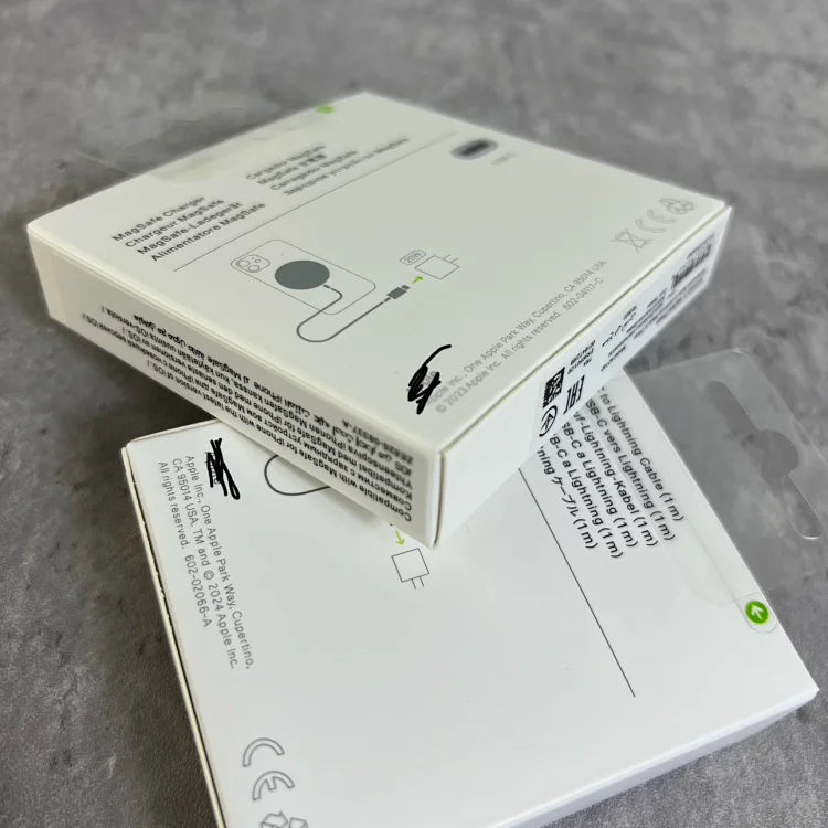 White Apple device packaging boxes stacked at an angle, showing product diagrams, text, and regulatory symbols on cardboard