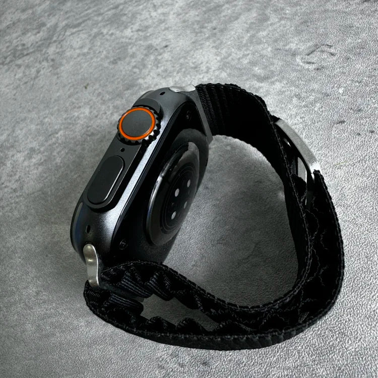 Black smartwatch with orange accent ring on digital crown, black fabric band, displayed on textured gray surface.