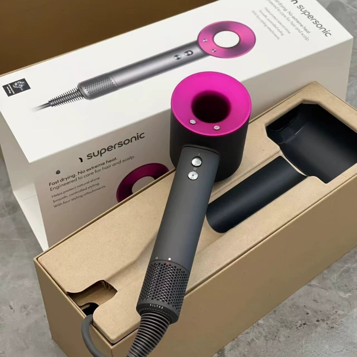 Dyson Supersonic hair dryer with gray barrel and magenta pink attachments displayed in beige packaging box with accessories