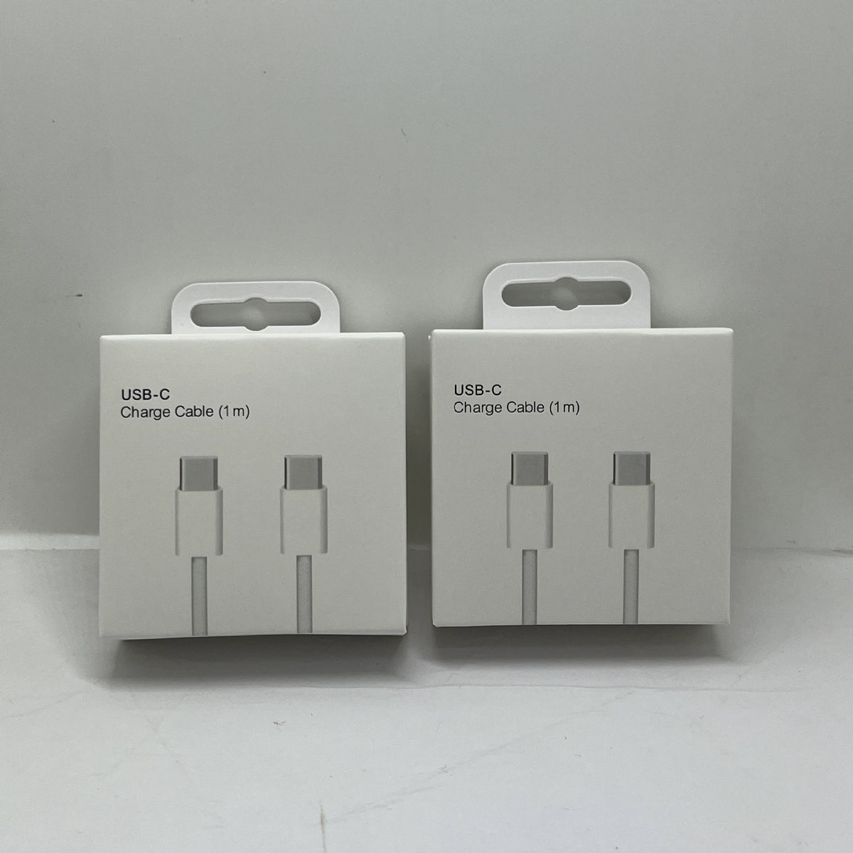 Two white USB-C charging cable boxes displayed side by side on a gray surface, each showing illustrations of gray and white